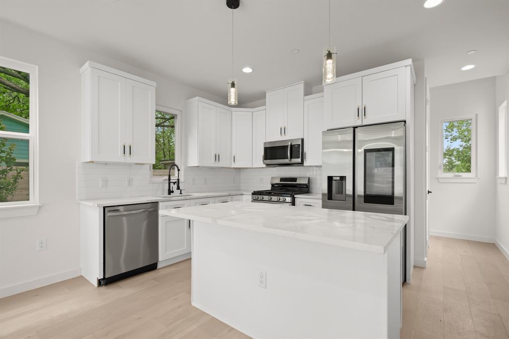 5305 Ledesma Road, Unit 4 Austin, TX 78721 - Photo 7 of 27 a kitchen with stainless steel appliances a refrigerator stove a sink and white cabinets with wooden floor