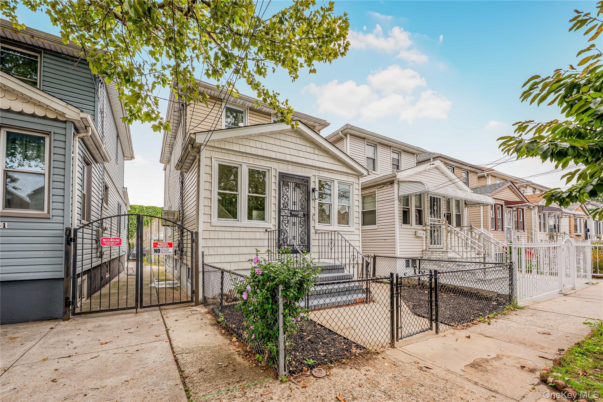 173-43 103rd Road Queens, NY 11433 - Photo 42 of 43 Exterior featuring light-colored siding, a front porch with railing, a security screen door, and a wrought iron front fence