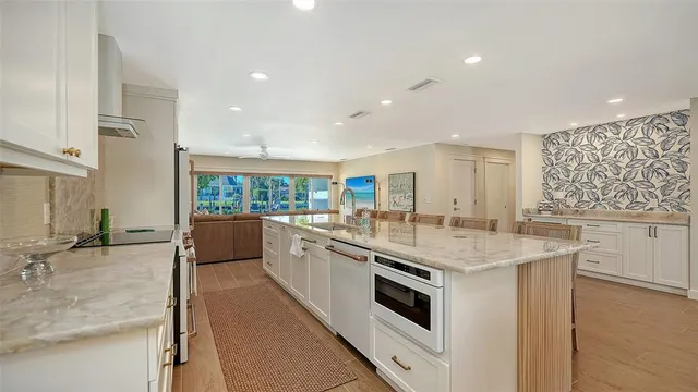 a kitchen with stainless steel appliances granite countertop a refrigerator a sink a stove and white cabinets with wooden floor