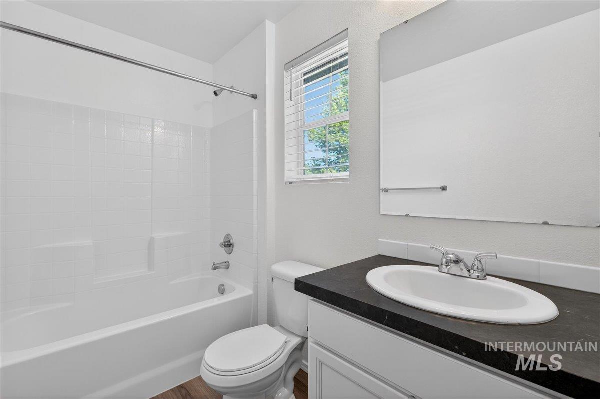 913 West Apple Pine Street Meridian, ID 83646 - Photo 22 of 32 Bathroom featuring a white bathtub with tile-effect surround, chrome shower fixtures, a single-pane window with blinds, wood-finish flooring, and a vanity with a dark countertop and white sink