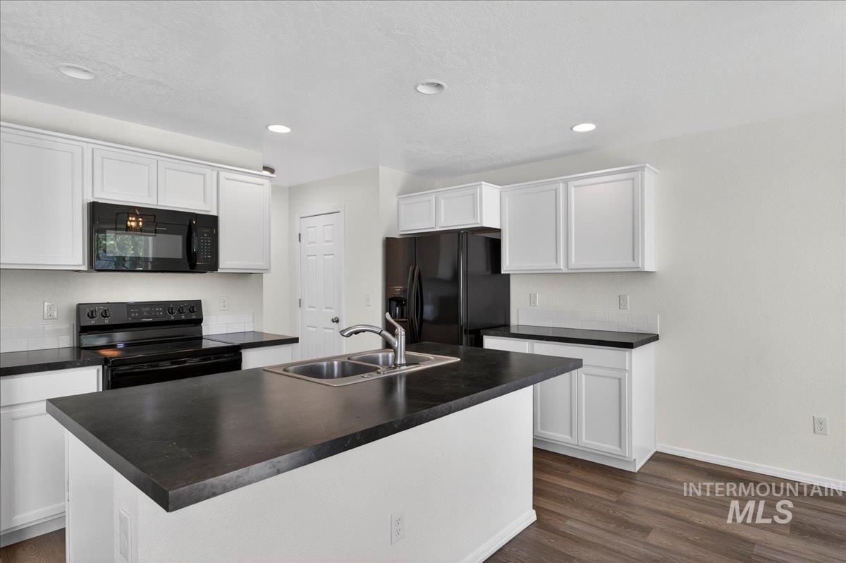 913 West Apple Pine Street Meridian, ID 83646 - Photo 10 of 32 Kitchen featuring an island with dual basin sink, white cabinetry, dark countertops, built-in microwave, and wood-finish flooring