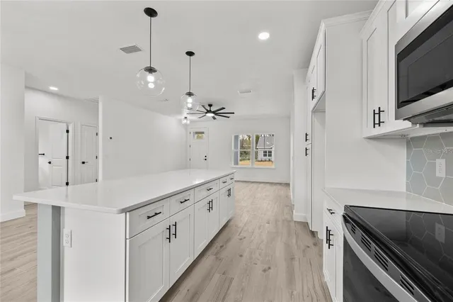a large white kitchen with a large counter top space a sink stainless steel appliances and cabinets