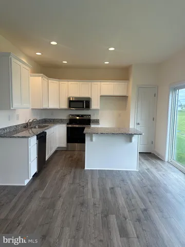 a kitchen with kitchen island granite countertop a stove top oven a sink and white cabinets with wooden floor