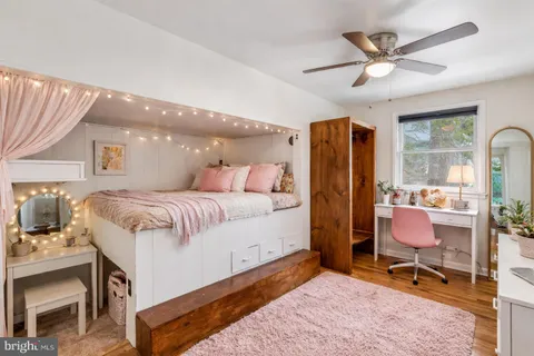 a bedroom with a bed a desk and chair with wooden floor