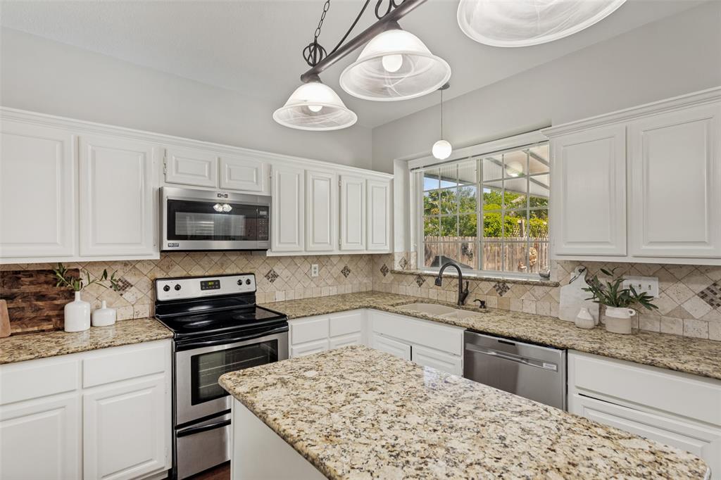 1228 Concho Drive Benbrook, TX 76126 - Photo 16 of 39 Kitchen featuring an island with granite countertops, white cabinetry, stainless steel appliances, and a tiled backsplash