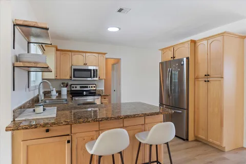 a kitchen with stainless steel appliances granite countertop a refrigerator a stove a sink dishwasher a dining table and chairs with wooden floor