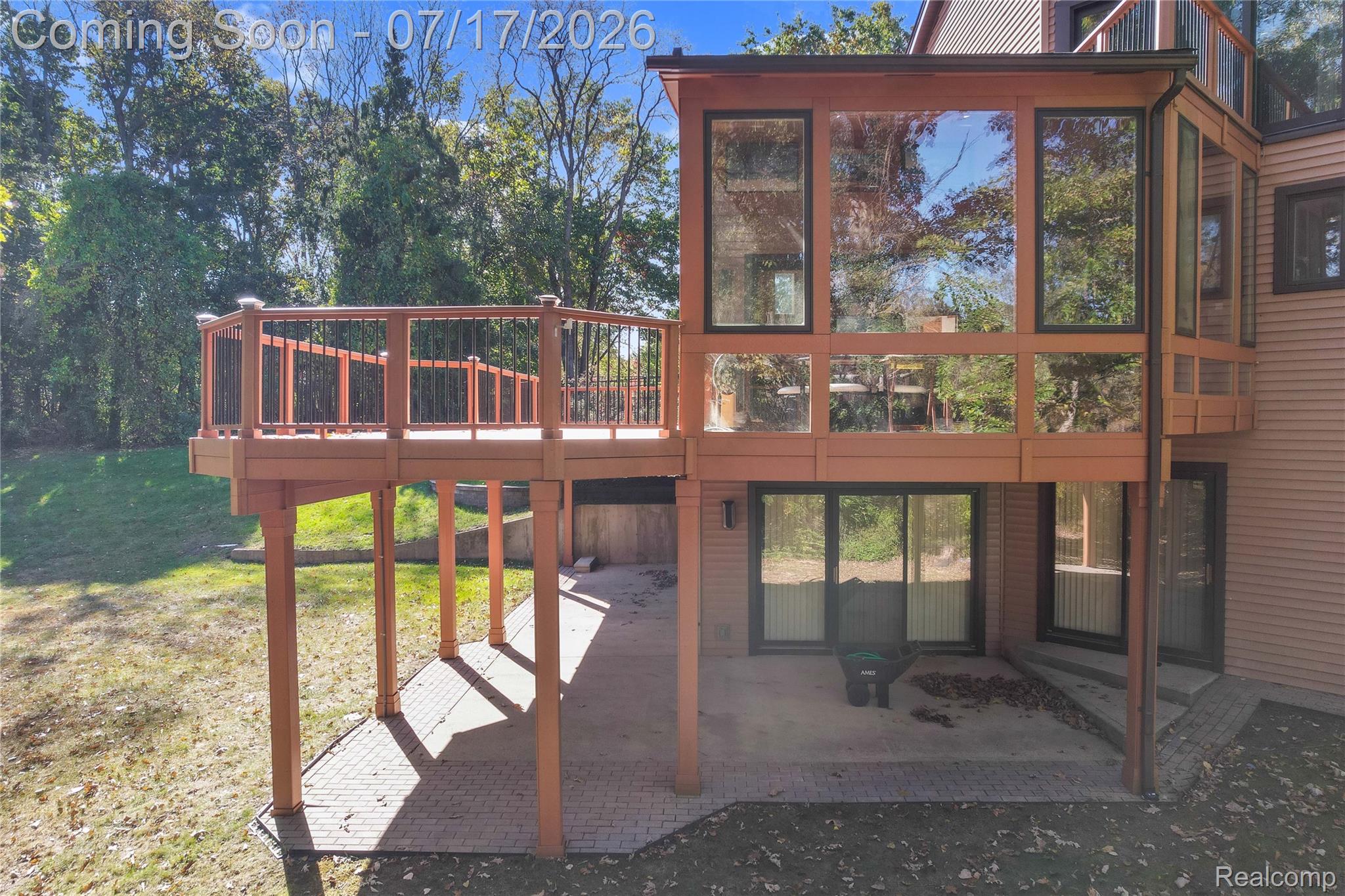 5685 Paint Valley Drive Rochester, MI 48306 - Photo 34 of 66 Multi-level exterior featuring a ground-level patio with stone pavers, a second-story wood-finish deck with black spindle railings, and a sunroom with expansive windows