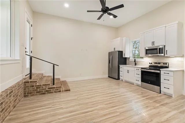 a kitchen with granite countertop a refrigerator oven a sink dishwasher and white cabinets with wooden floor