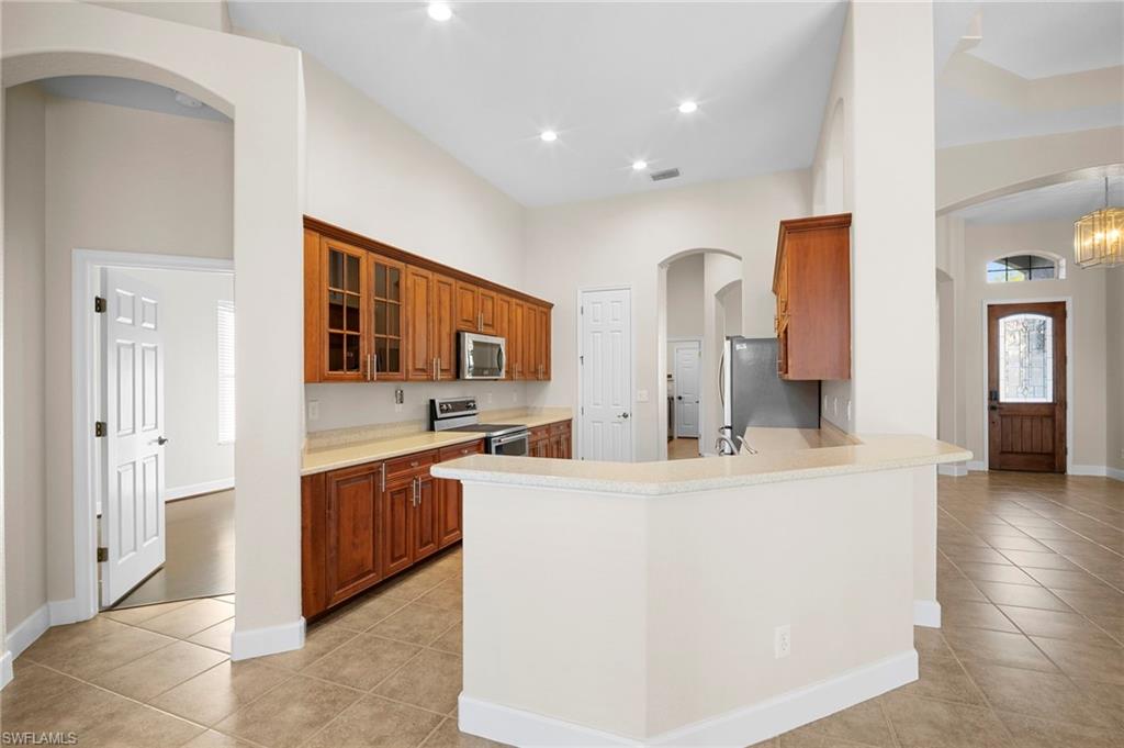 7915 Founders Circle Naples, FL 34104 - Photo 4 of 25 Kitchen featuring brown cabinets, arched walkways, a peninsula, stainless steel appliances, and light tile patterned flooring