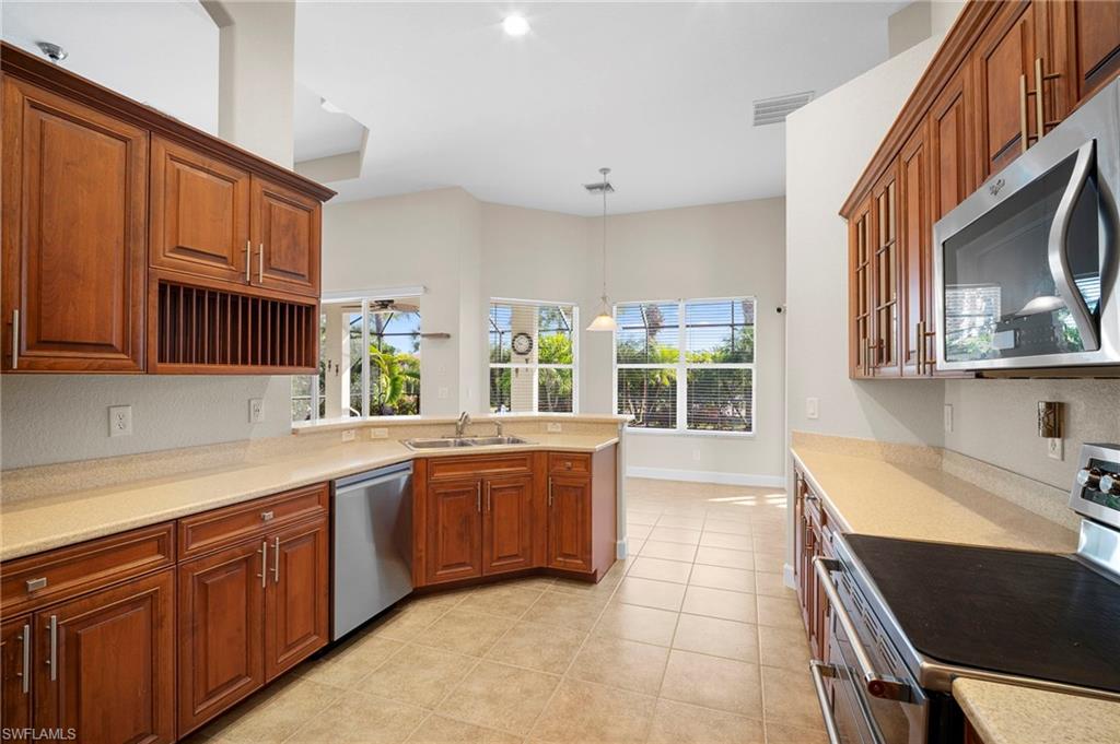 7915 Founders Circle Naples, FL 34104 - Photo 5 of 25 Kitchen with appliances with stainless steel finishes, decorative light fixtures, a peninsula, and brown cabinets