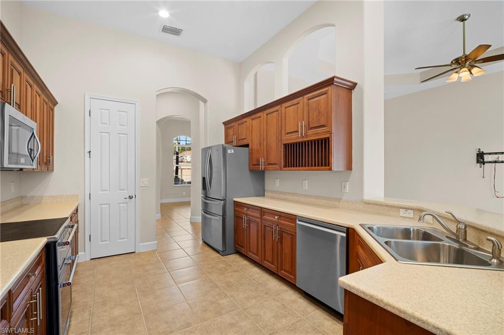 7915 Founders Circle Naples, FL 34104 - Photo 6 of 25 Kitchen featuring stainless steel appliances, light tile patterned flooring, brown cabinetry, a ceiling fan, and arched walkways