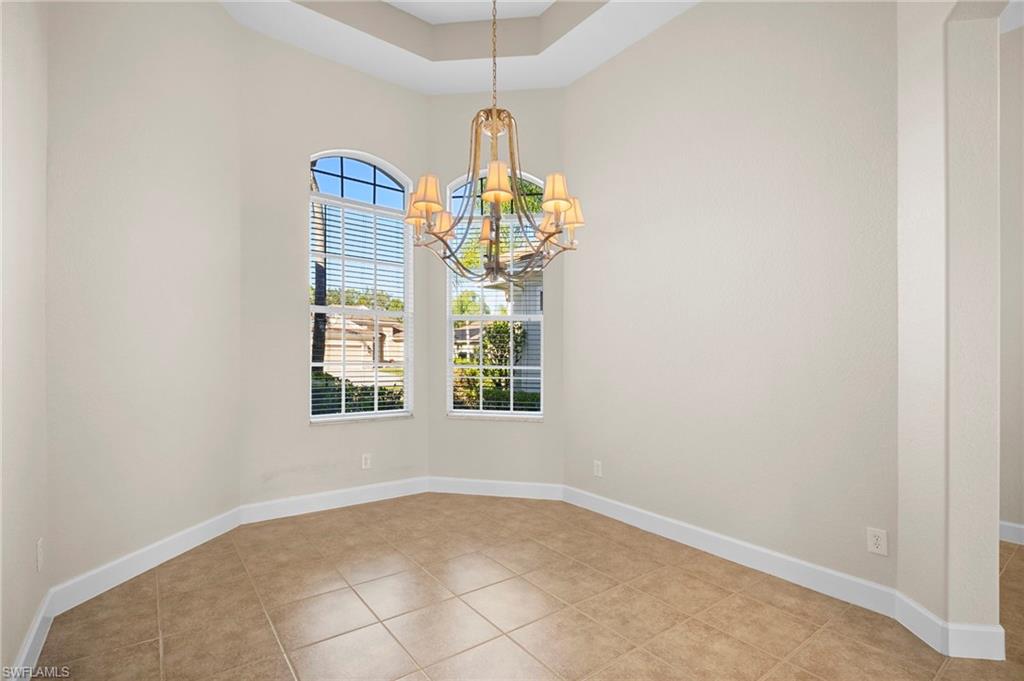 7915 Founders Circle Naples, FL 34104 - Photo 8 of 25 Empty room with a chandelier, a tray ceiling, and light tile patterned flooring