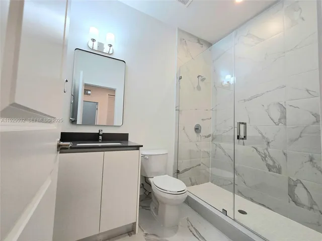 a bathroom with a granite countertop toilet a sink a mirror and shower