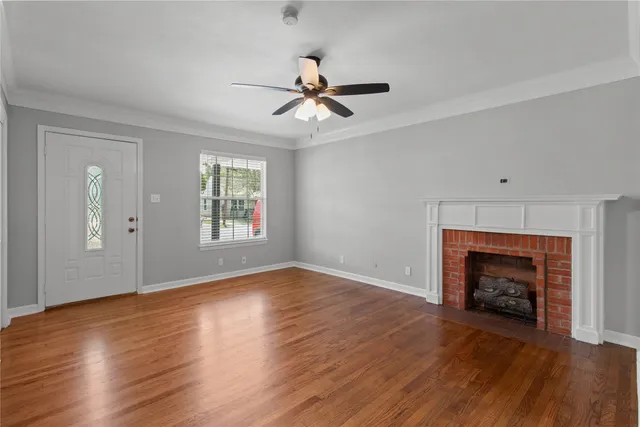 an empty room with wooden floor fireplace and a ceiling fan