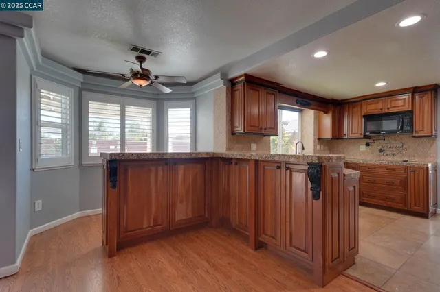 a kitchen with stainless steel appliances granite countertop a refrigerator a sink dishwasher a stove and a microwave oven on the wooden floor