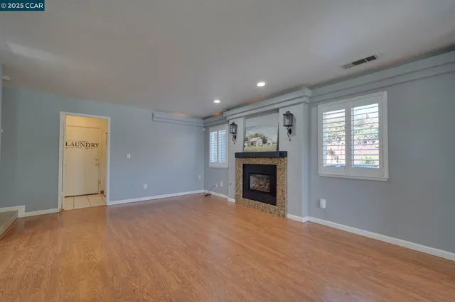 an empty room with wooden floor fireplace and windows