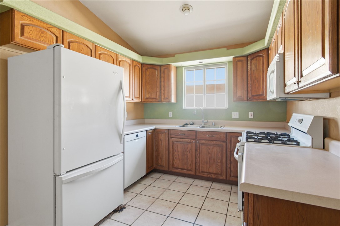 3740 North Kenneth Road Kingman, AZ 86409 - Photo 8 of 26 Kitchen with white appliances, light countertops, brown cabinetry, light tile patterned floors, and vaulted ceiling