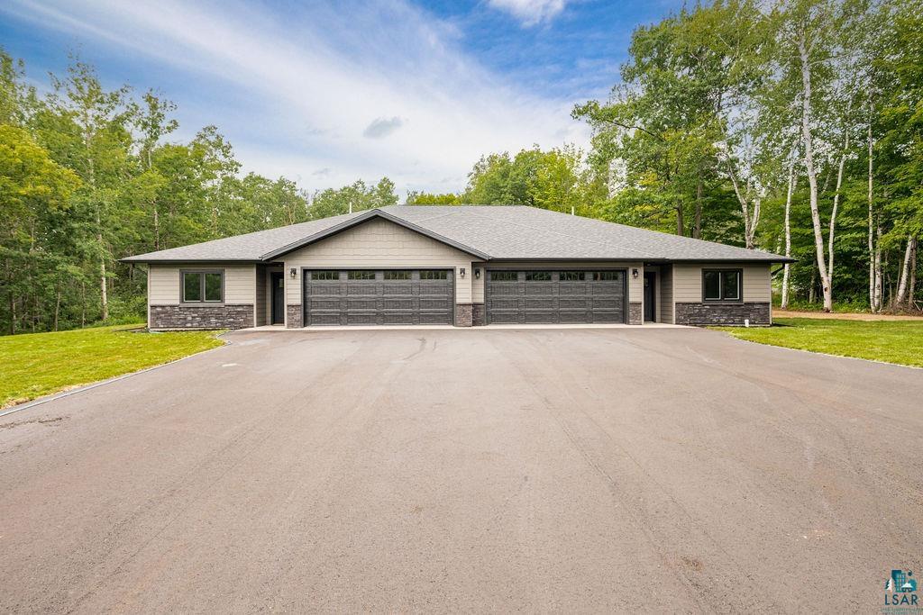 3971 Haines Road Hermantown, MN 55811 - Photo 2 of 34 Duplex exterior featuring light gray siding, dark gray stone accents, and dual two-car garages with carriage-style doors