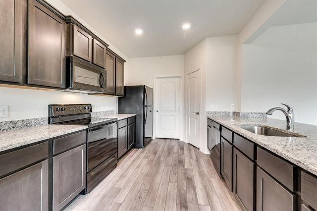 13609 Mineral Road Ponder, TX 76259 - Photo 5 of 21 Kitchen featuring extensive dark cabinetry, light granite countertops, stainless steel sink with gooseneck faucet, black appliances, and wood-finish flooring