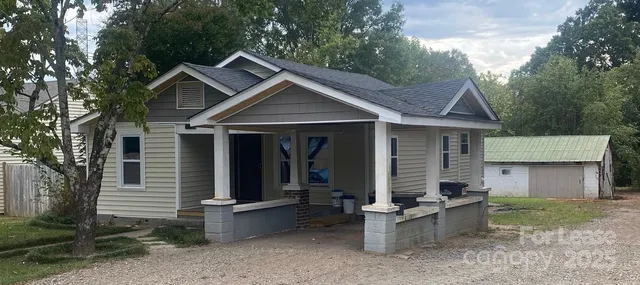 a view of a white house with a small yard plants and large tree