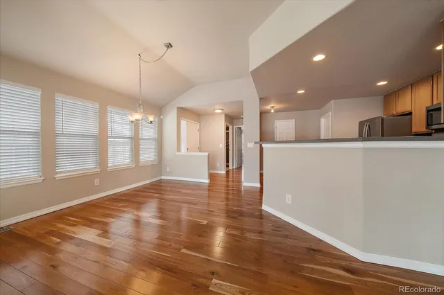 a view of an empty room and kitchen with wooden floor