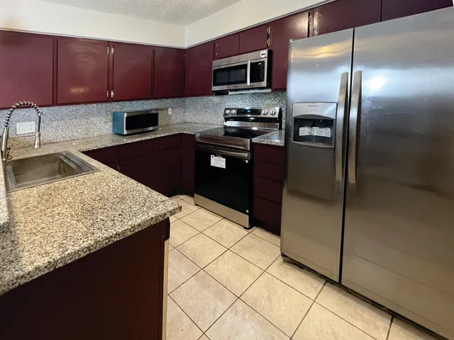 a kitchen with stainless steel appliances granite countertop a refrigerator a stove and a sink with wooden cabinets