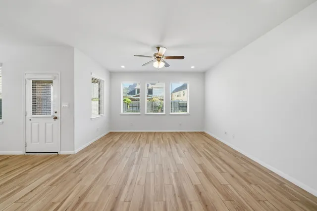 an empty room with wooden floor chandelier fan and windows