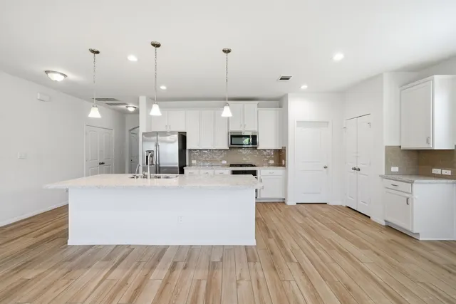 a large white kitchen with kitchen island a stove a sink dishwasher and a refrigerator with wooden floor
