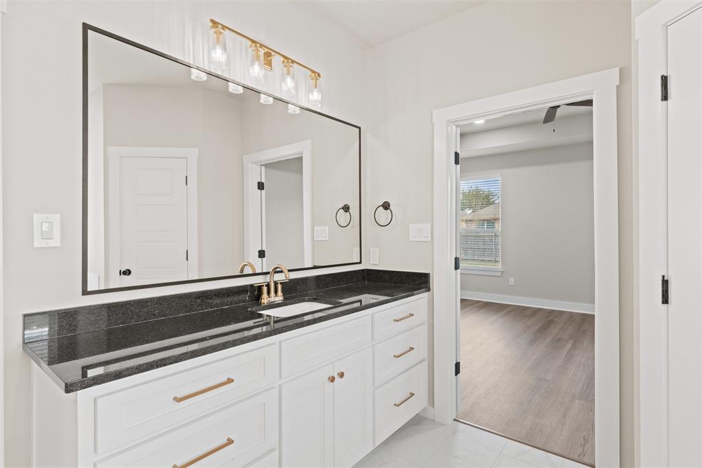 9824 Durango Trail Waco, TX 76712 - Photo 25 of 30 Bathroom vanity featuring a large mirror with a black frame, a dark stone countertop, and a white cabinet with gold-toned hardware