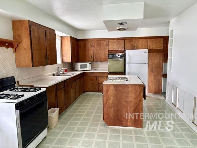 555 Cemetery Road Cambridge, ID 83610 - Photo 6 of 41 L-shaped kitchen with wood-finish cabinetry, solid surface countertops, and an integrated kitchen island with a drop-leaf extension