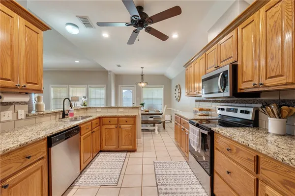a large kitchen with stainless steel appliances granite countertop a stove top oven a sink dishwasher a dining table and chairs with wooden floor