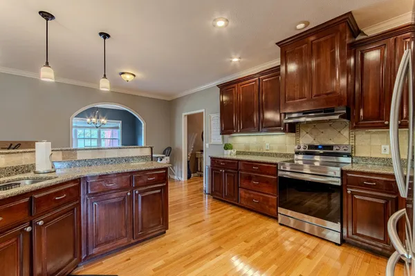 a kitchen with stainless steel appliances granite countertop wooden floors wooden cabinets a sink and a island