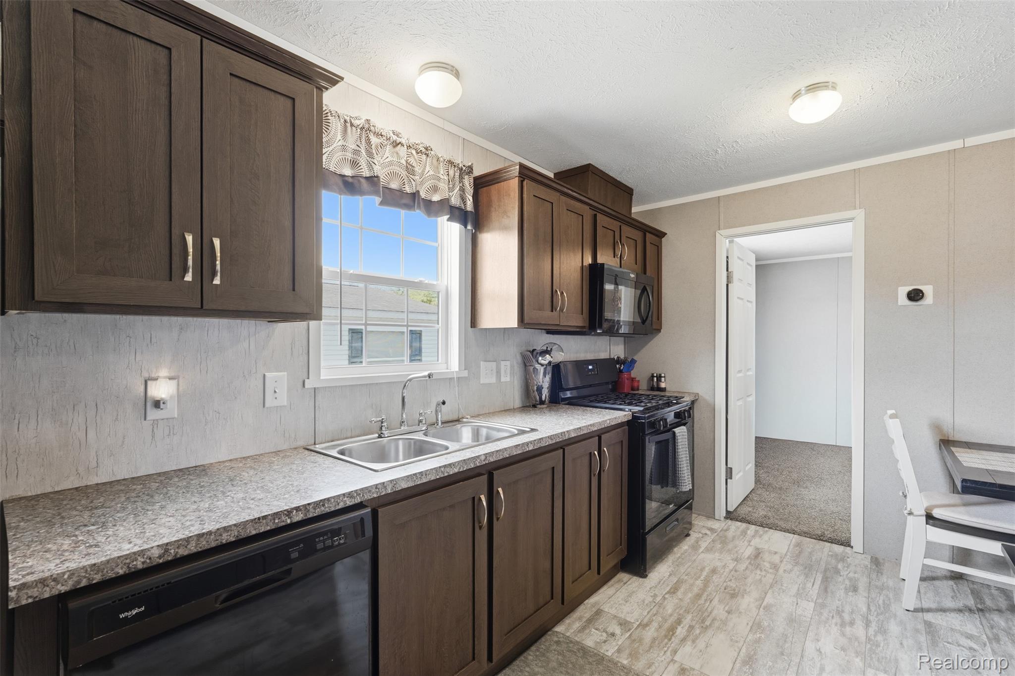 92 Normandy Drive Howell, MI 48843 - Photo 6 of 24 Kitchen featuring wood-finish cabinetry, speckled countertops, a double basin stainless steel sink, and a black appliance suite including a dishwasher, range, and microwave