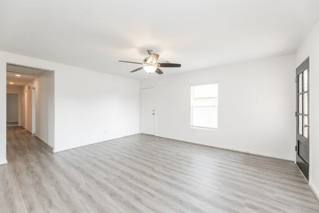 an empty room with wooden floor chandelier fan and windows