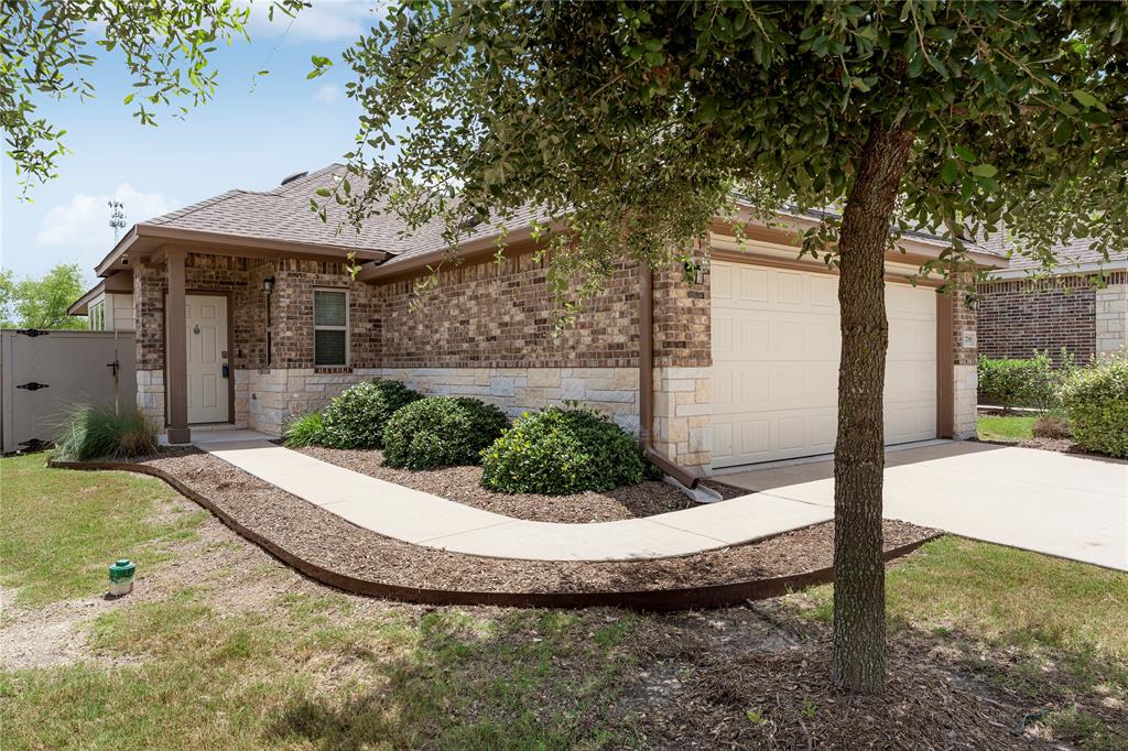 A curved concrete walkway leads past manicured landscaping to the brick entry and double garage.