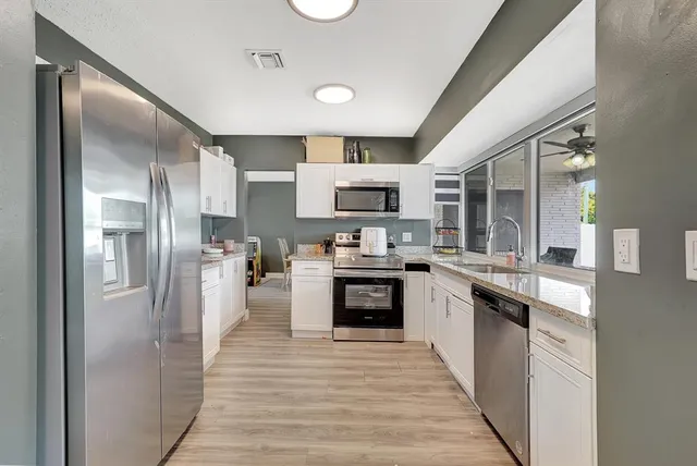 a kitchen with stainless steel appliances granite countertop a refrigerator a stove and a sink with wooden floor