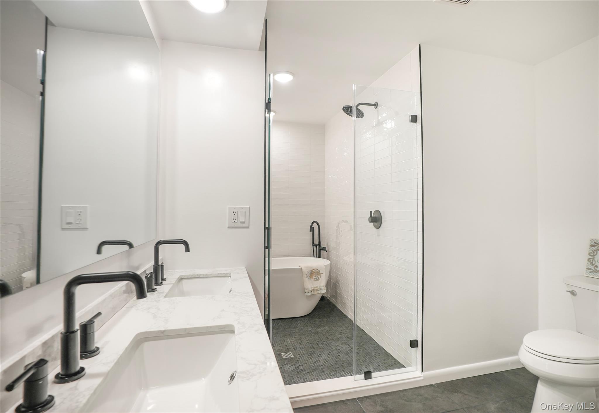 22 Peters Lane Pound Ridge, NY 10576 - Photo 21 of 43 Spacious bathroom featuring a dual vanity with white countertop, matte black fixtures, a walk-in shower with clear glass enclosure, a freestanding soaking tub, and a toilet