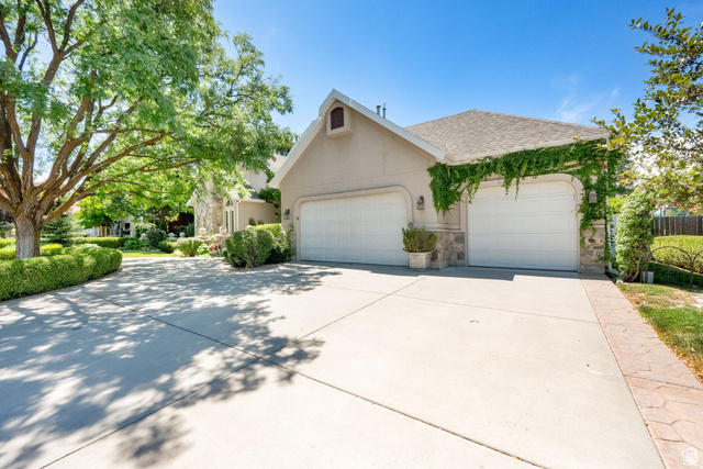 7740 Keswick Road Sandy, UT 84093 - Photo 6 of 74 Exterior featuring a two-car garage with white doors, stucco siding, stone accents, and climbing vine foliage