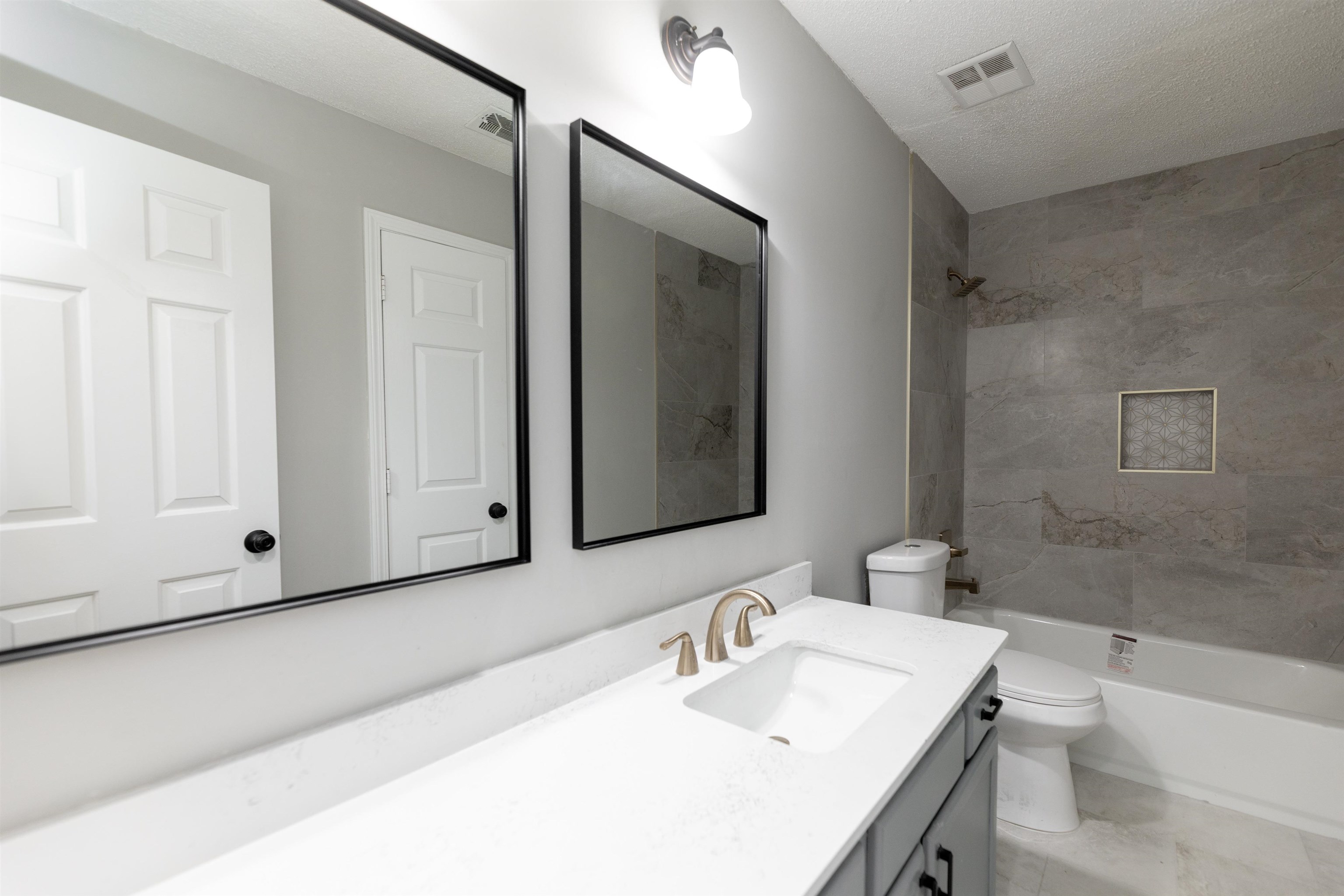7421 Richmond Road Memphis, TN 38125 - Photo 19 of 39 Bathroom featuring a vanity with an integrated sink, dual mirrors with black frames, a bronze-finish faucet, and a shower-tub combination with large format wall tiles and a recessed niche