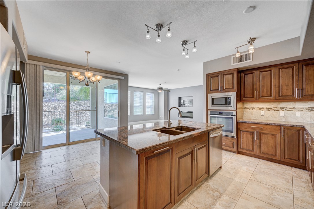 Kitchen featuring wood finish cabinets, hanging lights, stainless steel appliances, and a center island with sink