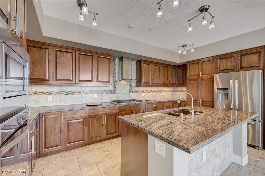 2555 Hampton Road, Unit 6108 Henderson, NV 89052 - Photo 10 of 63 Kitchen featuring wood finish cabinets, stainless steel appliances, light stone counters, an island with sink, and decorative backsplash