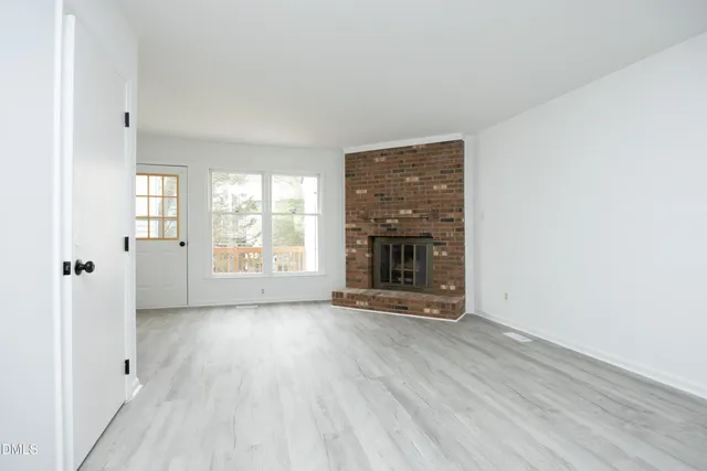 an empty room with wooden floor a fireplace and windows