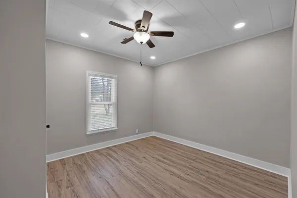 an empty room with wooden floor ceiling fan and windows