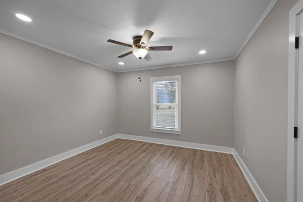 an empty room with wooden floor fan and windows