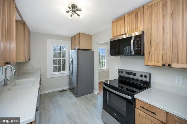 a kitchen with stainless steel appliances a sink a stove a microwave a refrigerator a window and cabinets