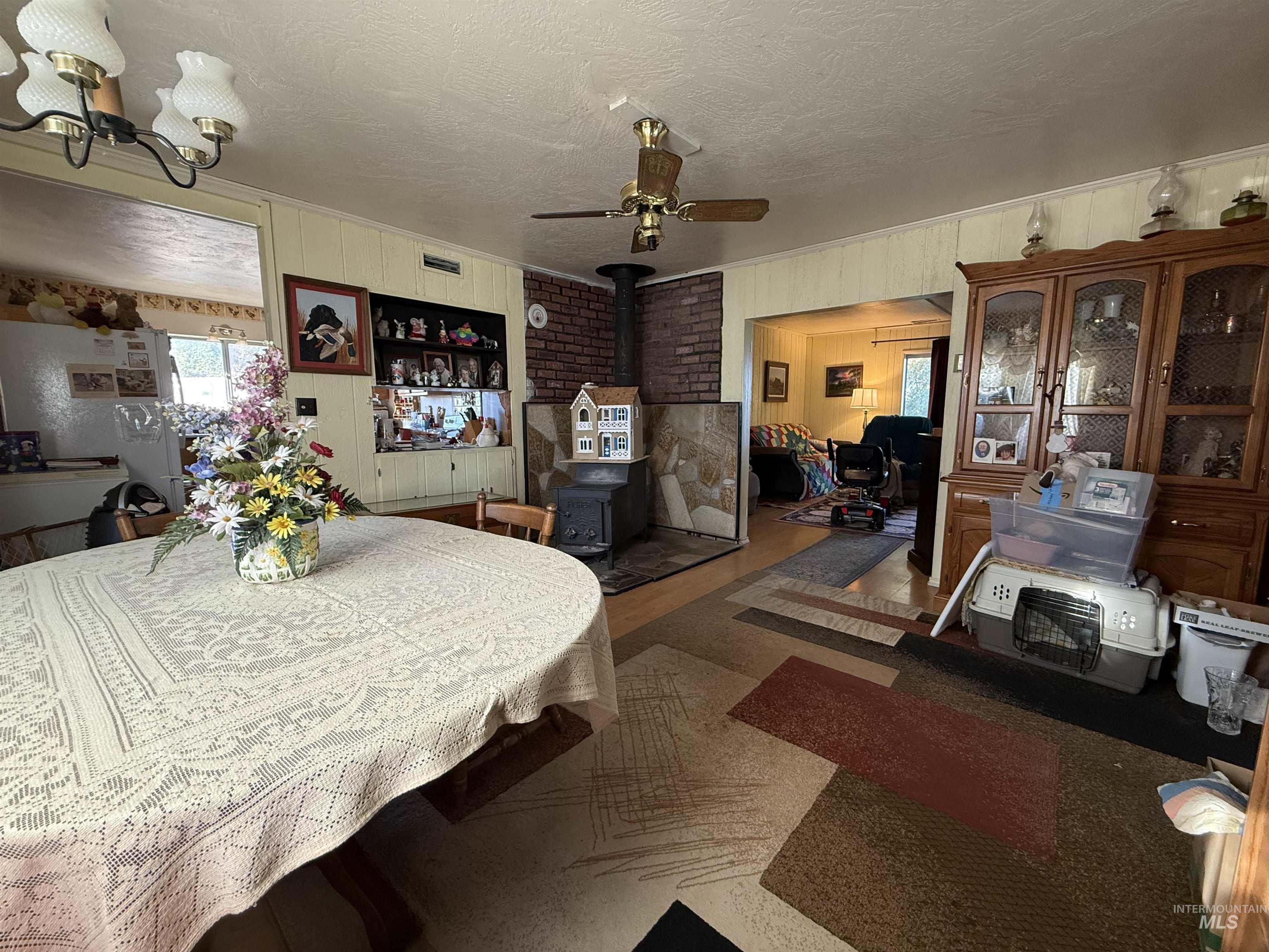 19241 West Homedale Road Caldwell, ID 83607 - Photo 20 of 35 Dining room featuring ceiling fan, a wood stove, a textured ceiling, a chandelier, and wooden walls