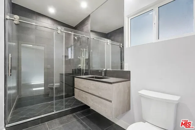 a bathroom with a granite countertop sink a toilet a mirror and shower