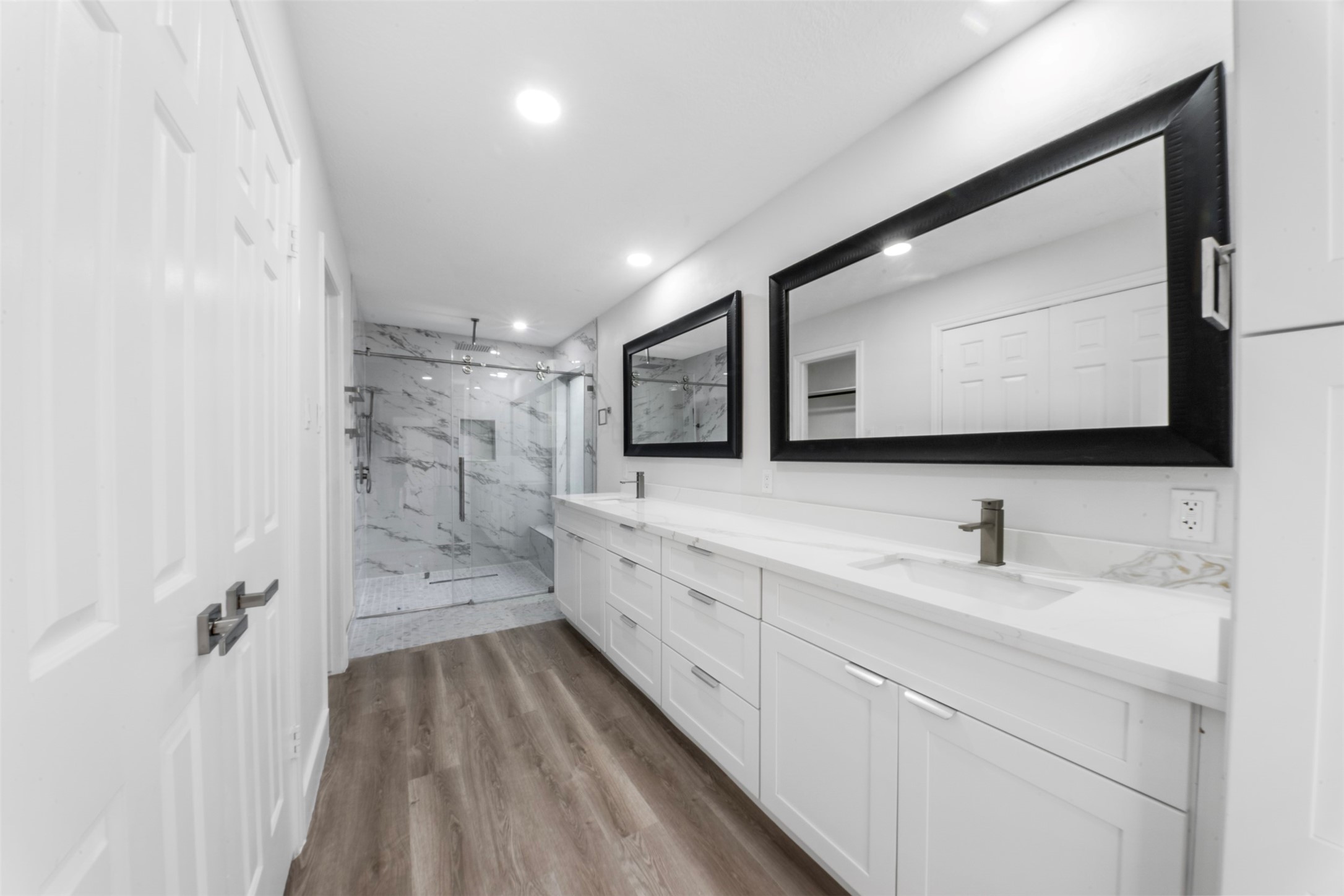 9543 Enstone Circle Spring, TX 77379 - Photo 20 of 50 This bathroom features a modern design with a spacious double vanity, large mirrors, and a sleek glass-enclosed shower. The light wood flooring and white cabinetry create a bright and inviting atmosphere.