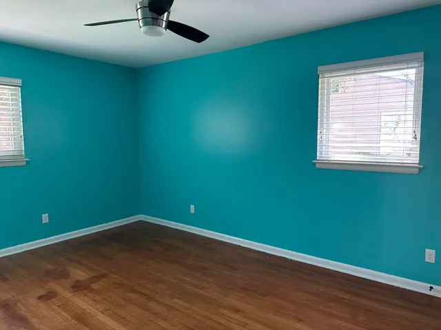 an empty room with wooden floor chandelier fan and windows