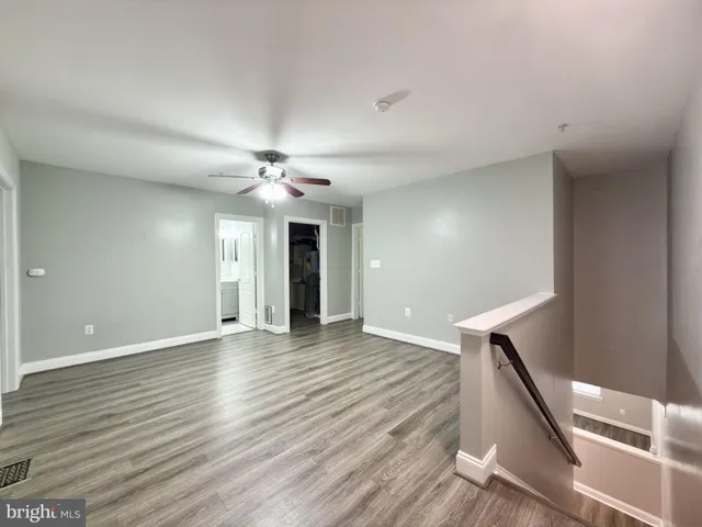 a view of an empty room with wooden floor and a ceiling fan